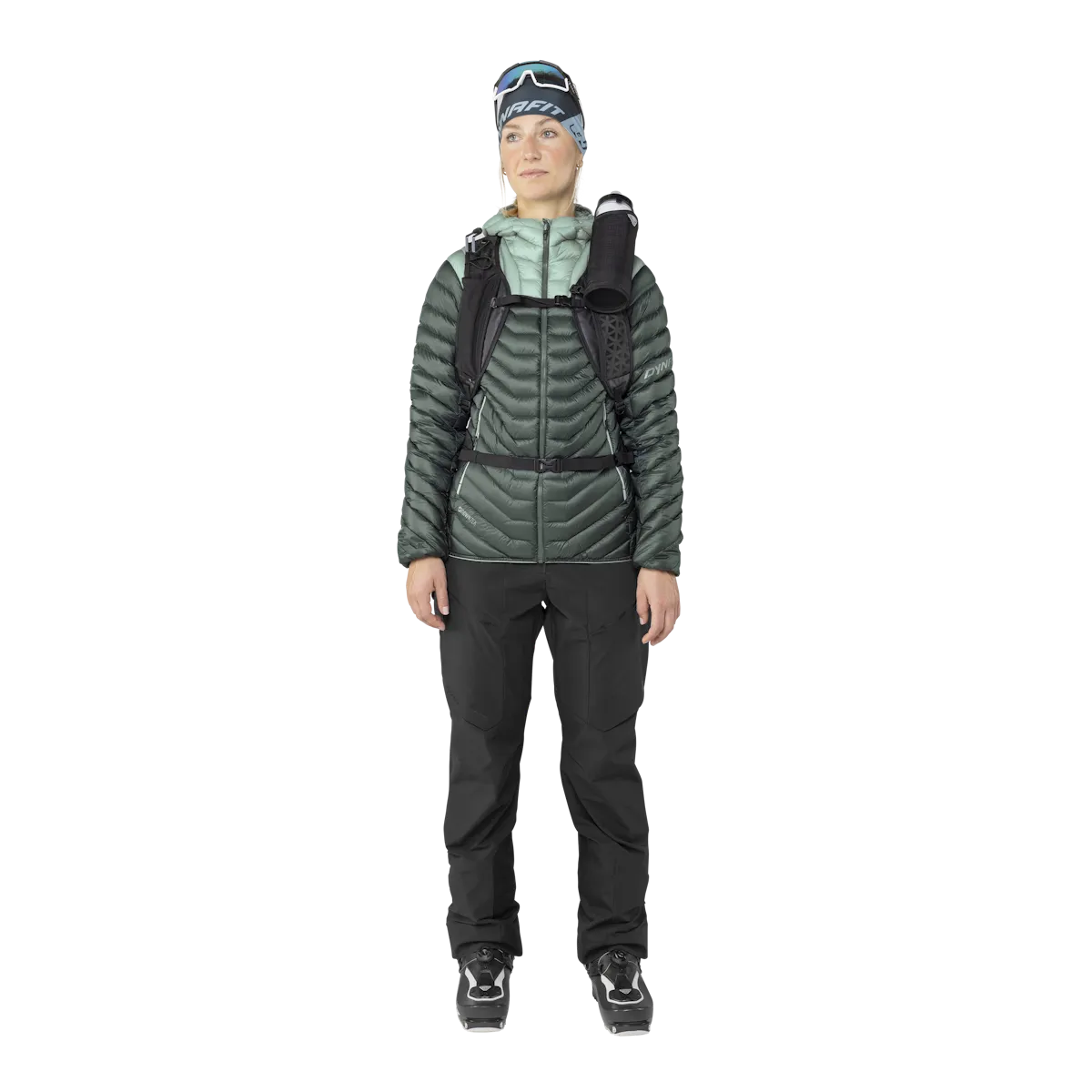 A woman in ski clothing, with Dynafit Ridge Ultralight down jacket in green, pants and ski boots.