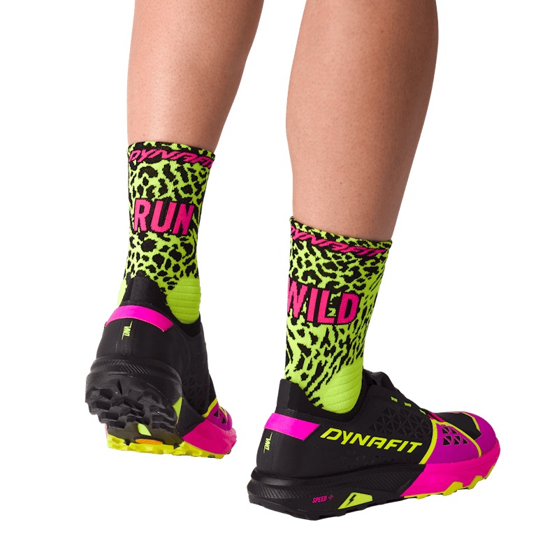 Beine in Socken mit "RUN" und "WILD", Neon-Leopardenmuster. Schwarze Laufschuhe mit pinken und gelben Akzenten.