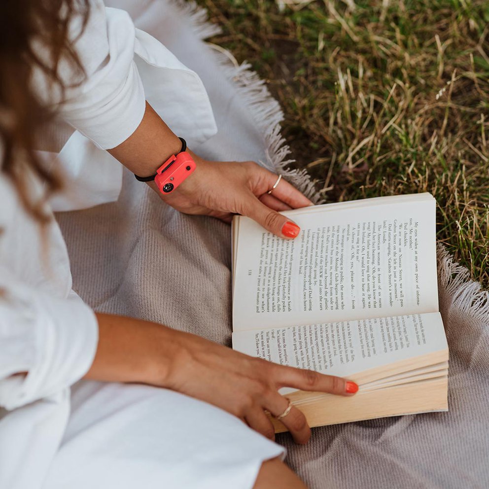 Aktives Lesen im Freien Person liest im Freien ein Buch mit "Tickless Active" am Handgelenk. Fokus auf den Schutz beim aktiven Lesen.