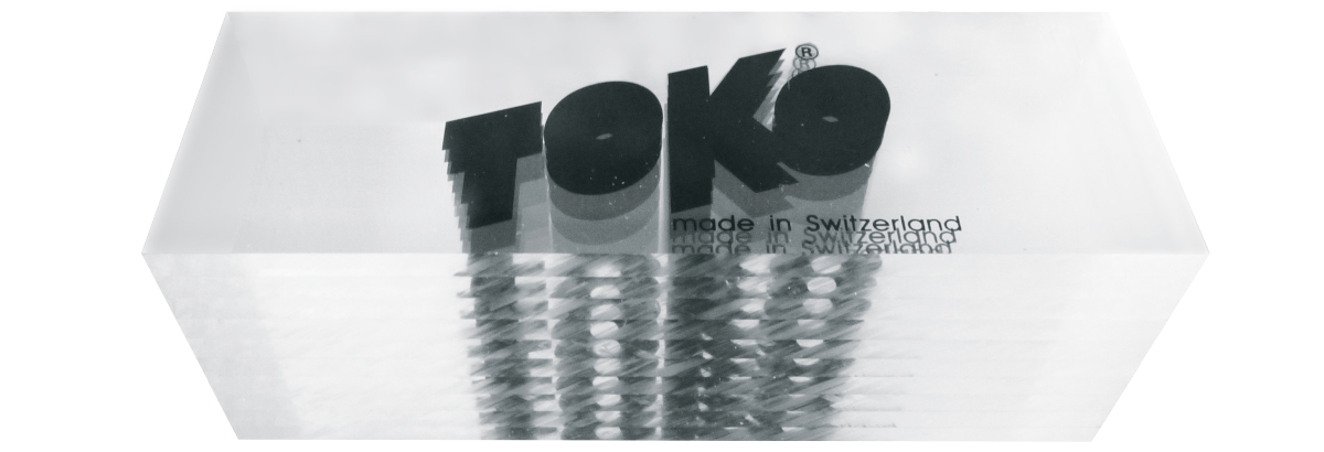 Das Bild zeigt 10 Toko Plexi Blades, gestapelt in Originalverpackung, mit Logo und Herkunftsangabe "made in Switzerland".