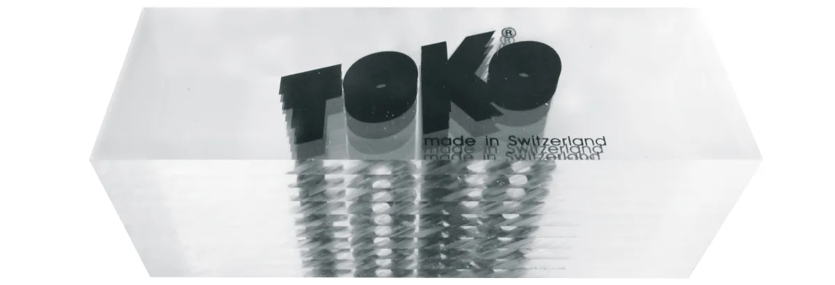 Das Bild zeigt 10 Toko Plexi Blades, gestapelt in Originalverpackung, mit Logo und Herkunftsangabe "made in Switzerland".
