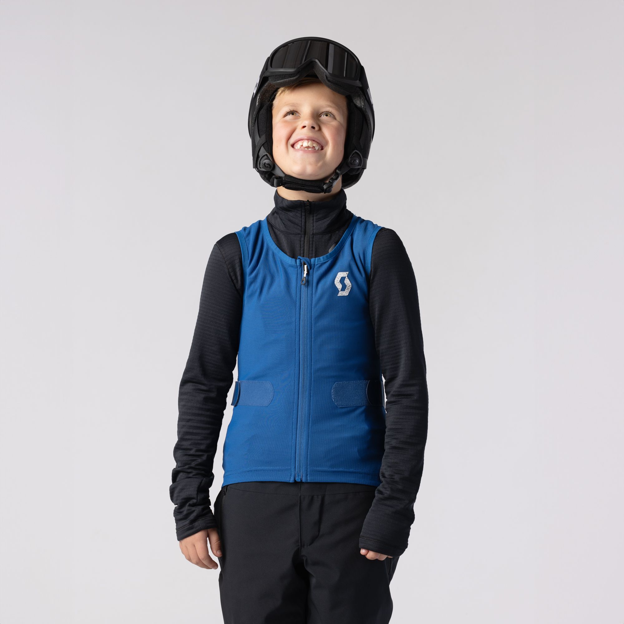Ragazzo sorridente con gilet Scott Un ragazzo sorridente con casco e occhiali da sci indossa un gilet blu Scott Airflow Junior.