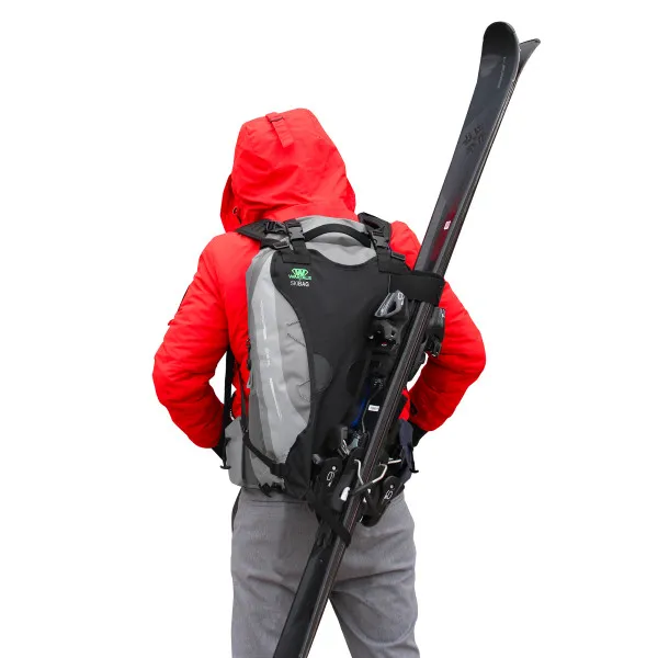 Person with ski backpack carrying skis. The backpack is gray-black. The person is wearing a red jacket.