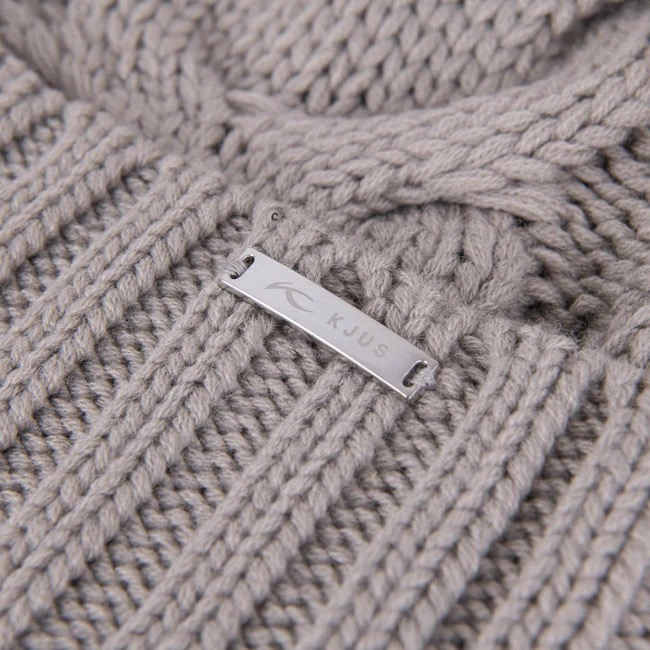 Gros plan sur un bonnet gris clair en tricot avec un motif torsadé et une étiquette argentée avec le logo "KJUS".