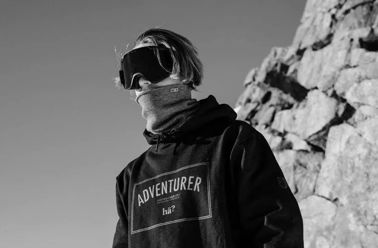Black and white photo: person with ski goggles and Drifter Merino neck warmer against a rocky background.