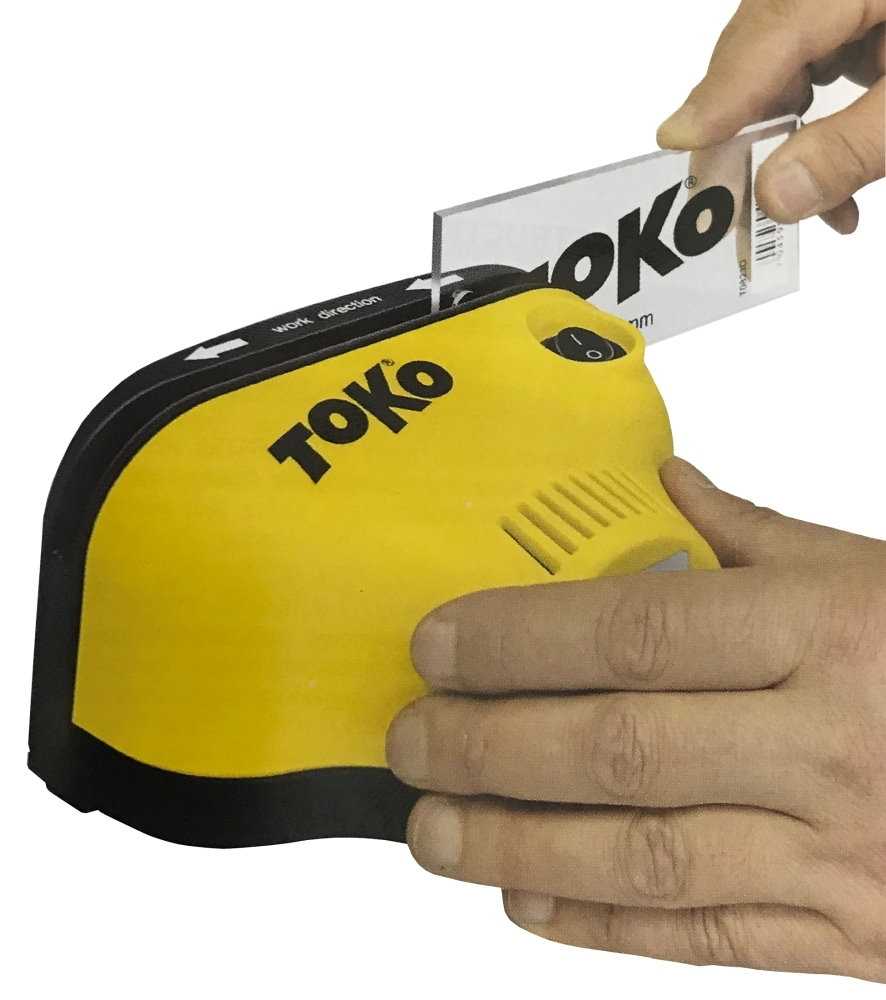 Gelber Toko Scraper Sharpener Pro in Benutzung. Eine Hand führt den Schaber durch die Öffnung.