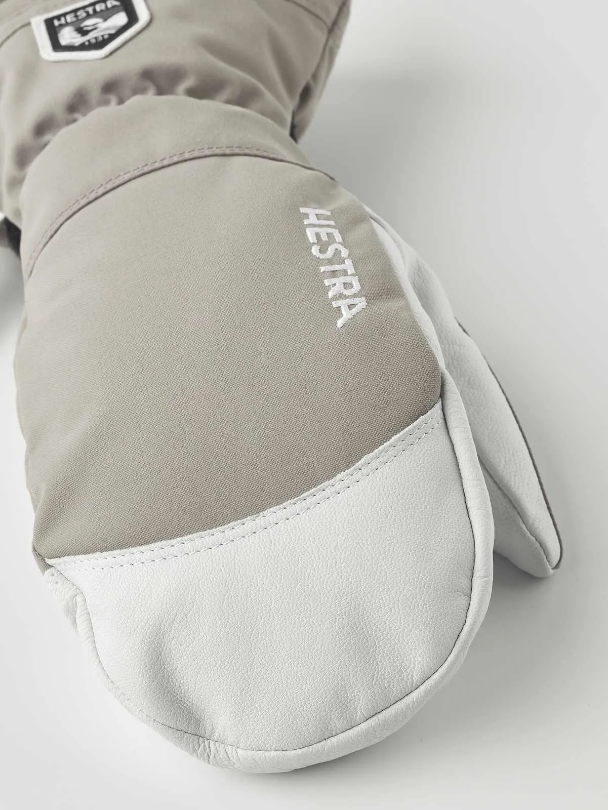 Nahaufnahme eines hellbraunen Hestra Army Leather Heli Ski Mitt Fausthandschuhs mit weißem Leder an der Spitze.