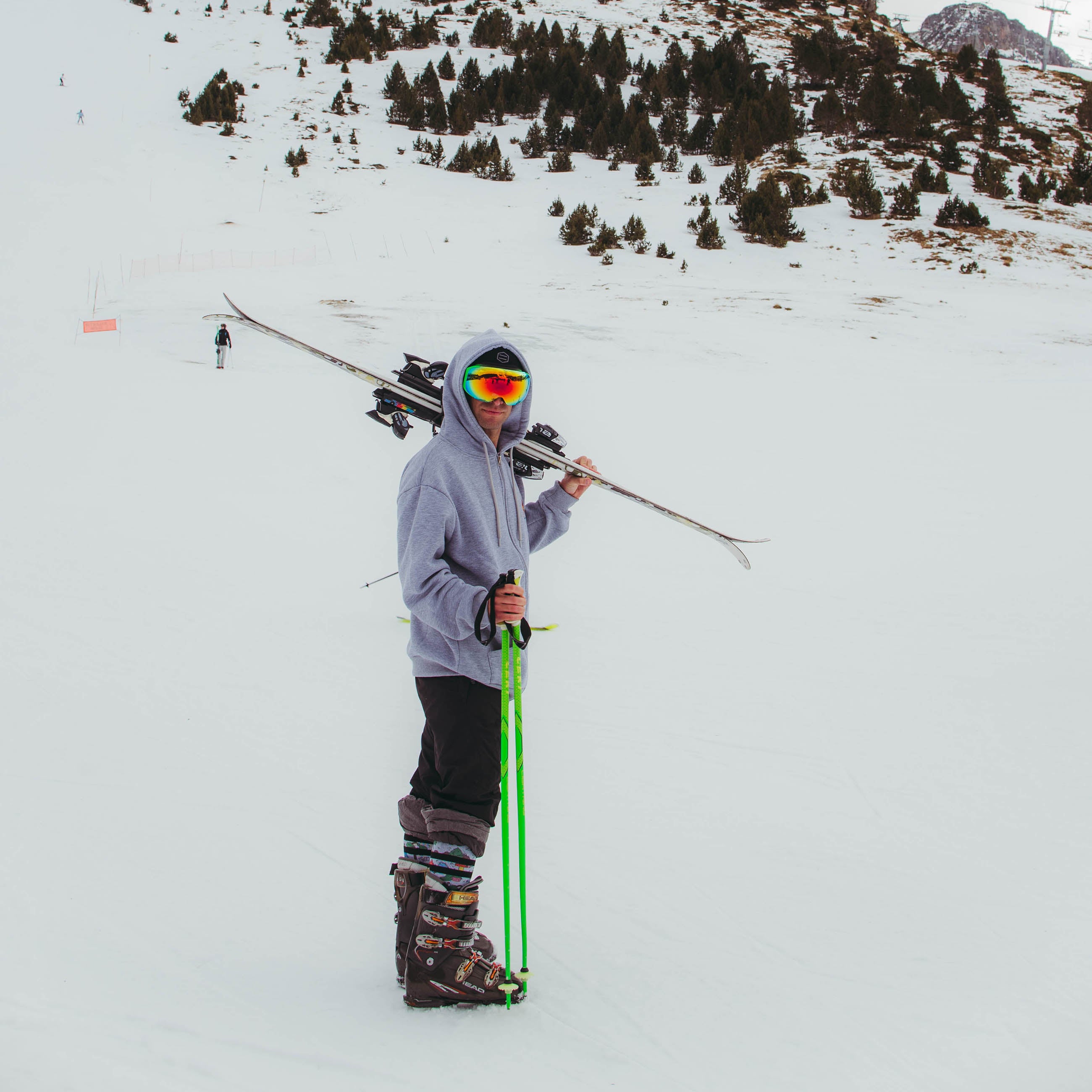 Skifahrer mit Snow Socks Mann mit Skiern, Skistöcken und Schneebrille auf einer verschneiten Piste. Er trägt Leaf Me Alone Snow Socks.