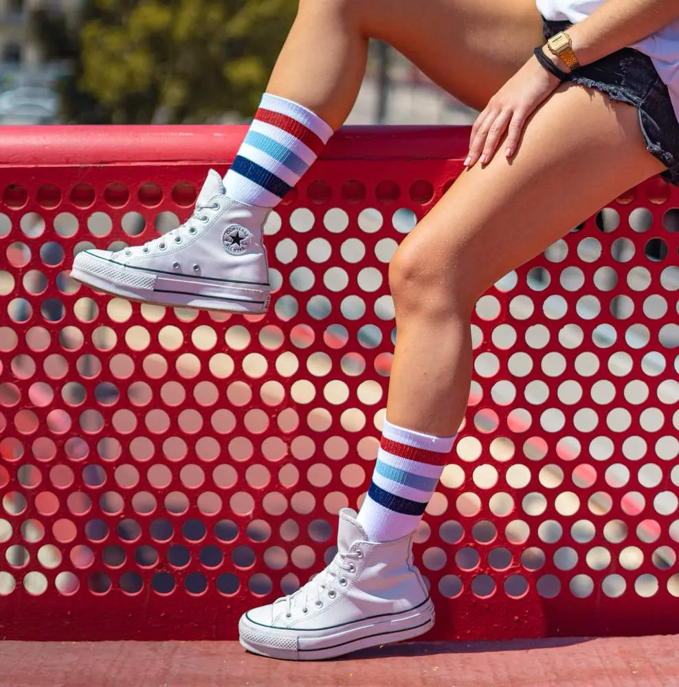Person with McFly II Mid High socks and white shoes against a red background.