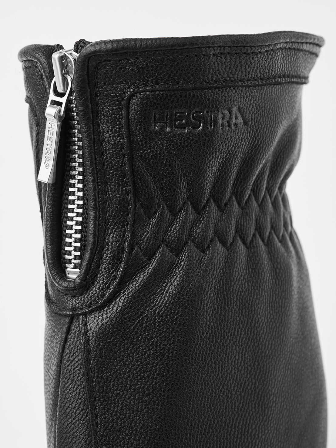 Detailaufnahme eines schwarzen Lederhandschuhs mit Reißverschluss und dem eingeprägten Markennamen „HESTRA“.