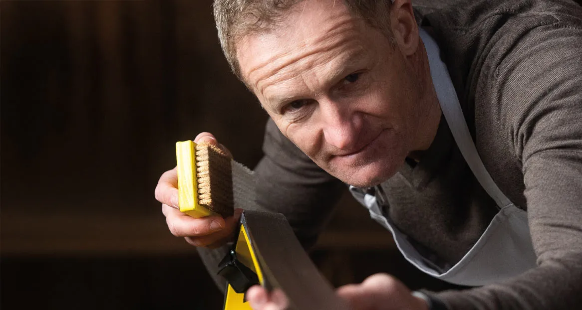 Un homme aux cheveux gris, tenant une brosse jaune à la main, prépare un ski.