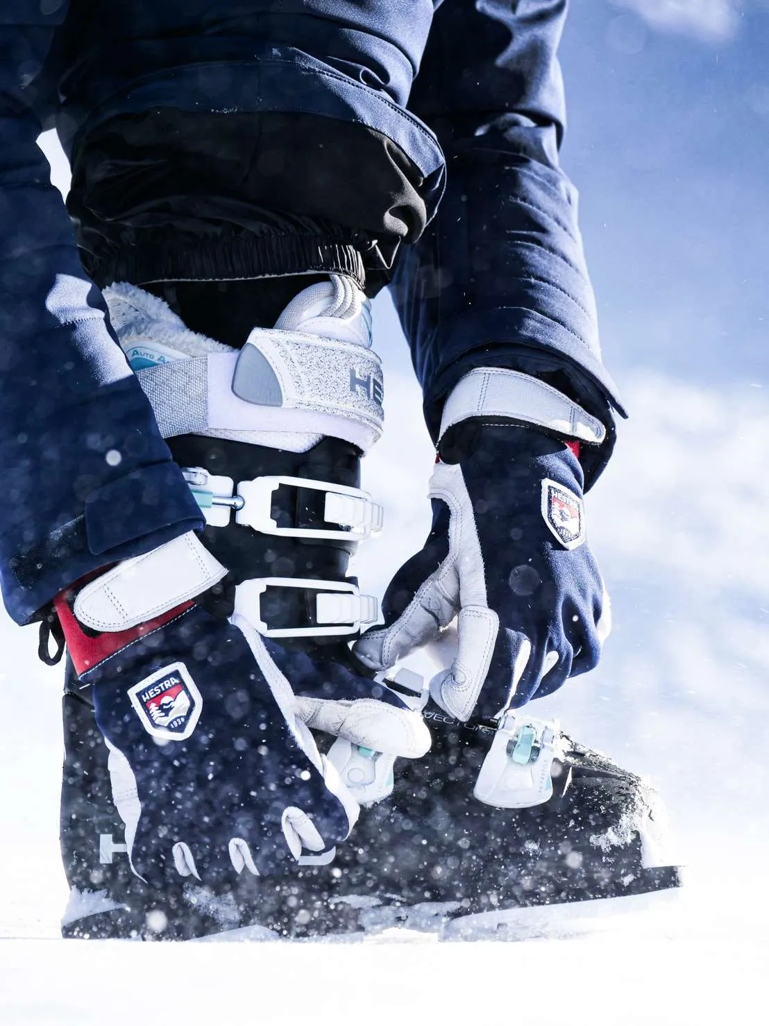 Le skieur ferme dans la neige avec Hestra-gants une chaussure de ski avec des boucles blanches.