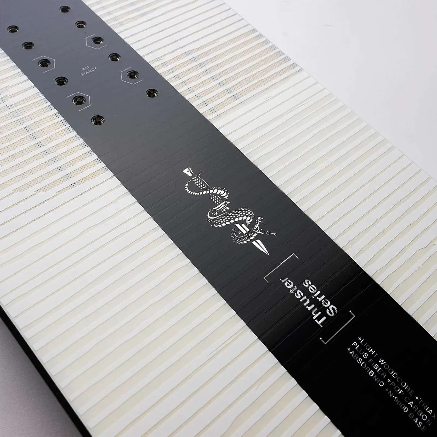 Vue détaillée Nidecker Thruster Snowboard : trous de fixation, graphisme de serpent sur planche à motifs noirs et blancs.