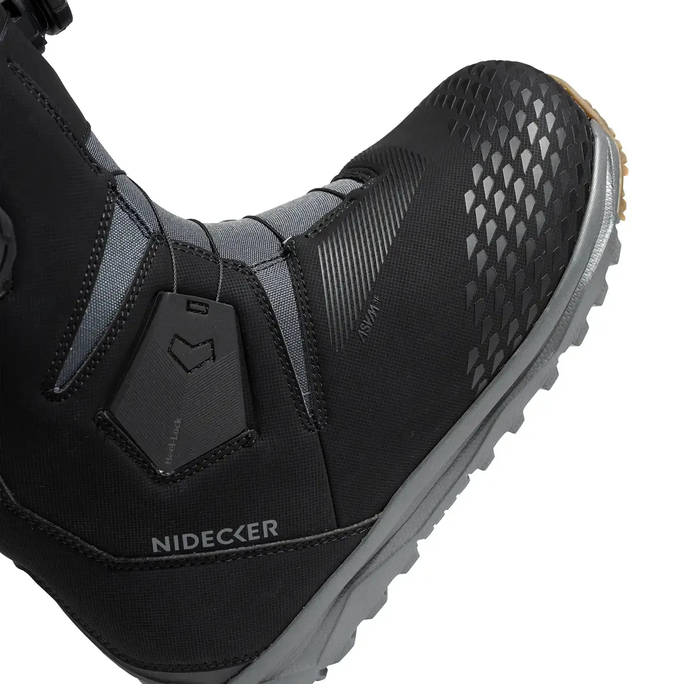 Detailed view of a black Nidecker snowboard boot with gray sole and Heellock system. The upper material has a diamond pattern.