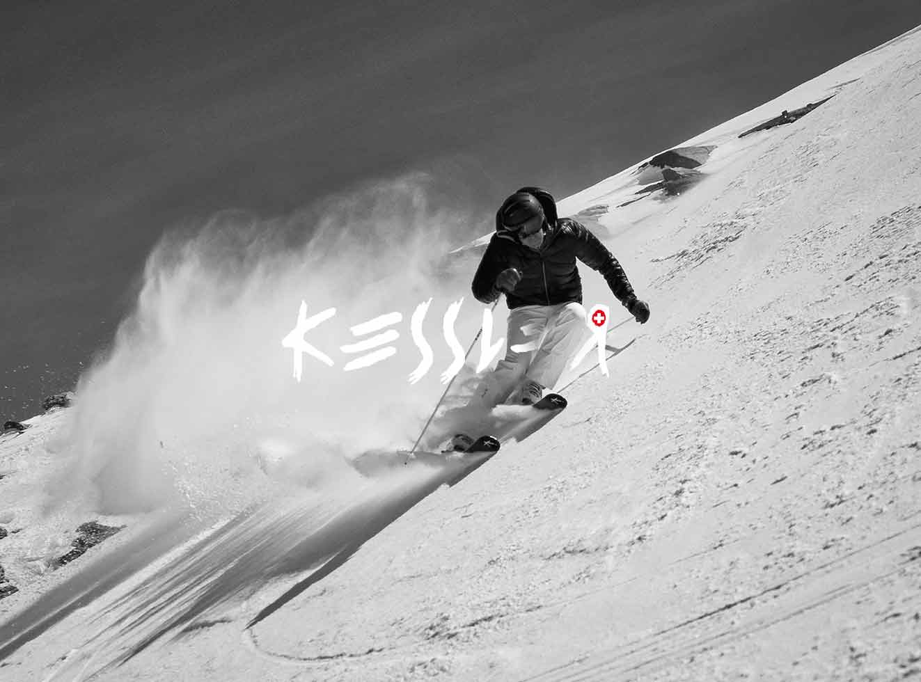Schwarz-weiß Aufnahme eines Skifahrers in voller Fahrt, Schnee wirbelt auf, „Kessler“ Schriftzug sichtbar.