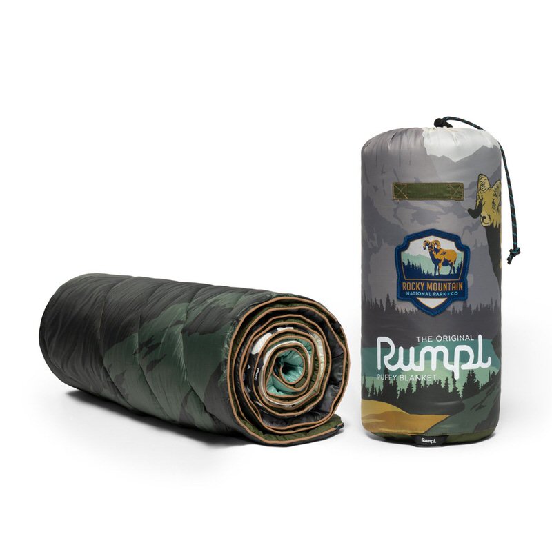 Gerollte Puffy-Decke mit Tarnmuster, daneben ein Packsack mit Rocky Mountain-Motiv.