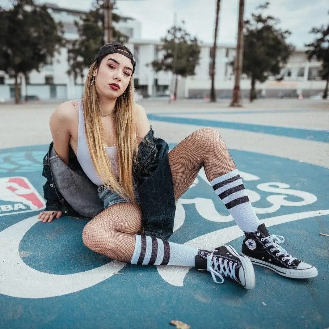 Model sitting, wearing mid-high socks with stripes, tights and sneakers on a blue background.