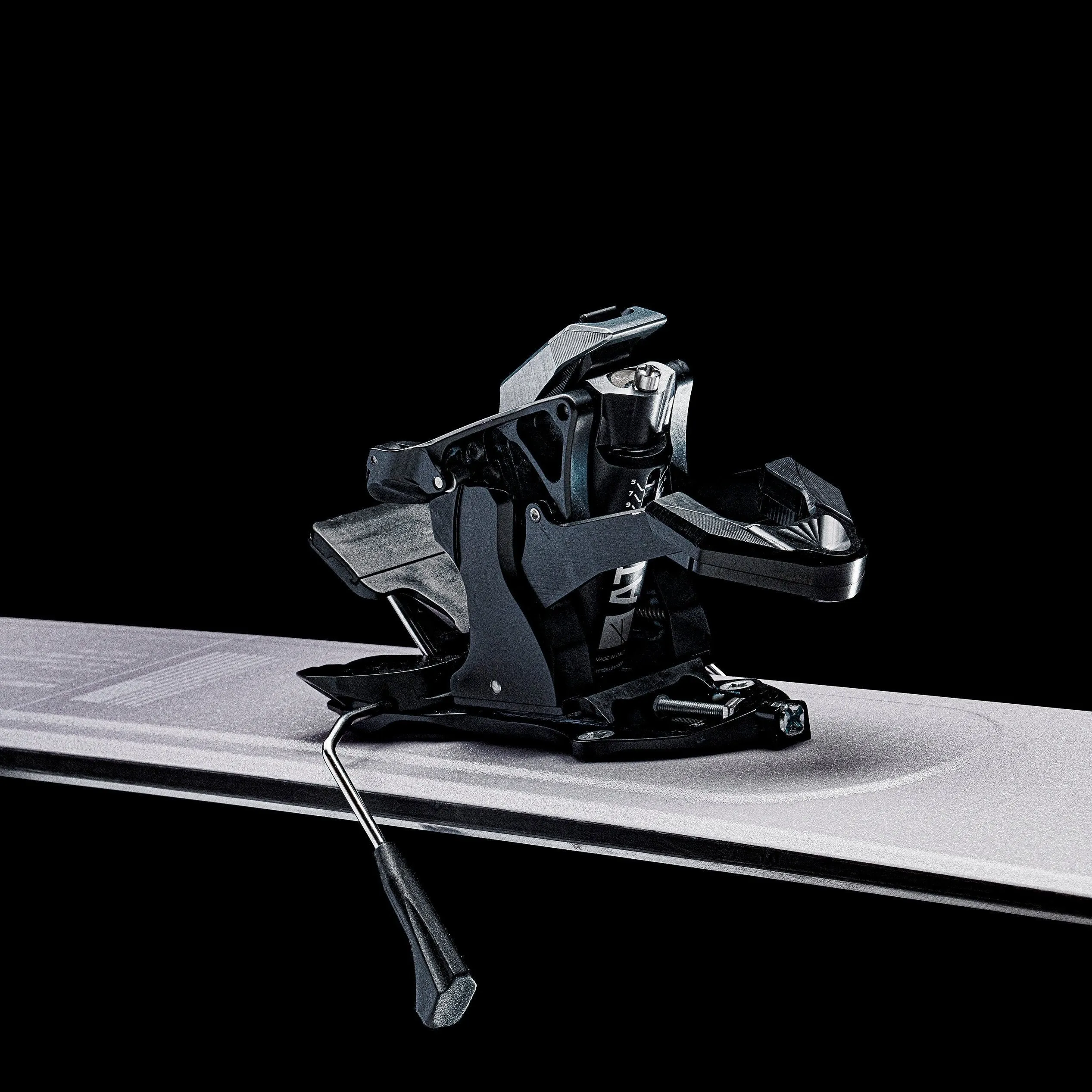 Close-up of a black ski binding on a ski against a black background.