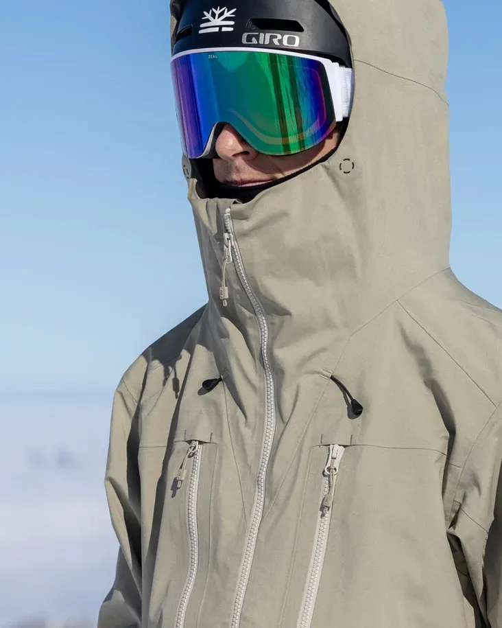 Persona con giacca Seneca Rock color Z-2 EPE 3L con cappuccio, casco e occhiali da sci davanti a un cielo blu.