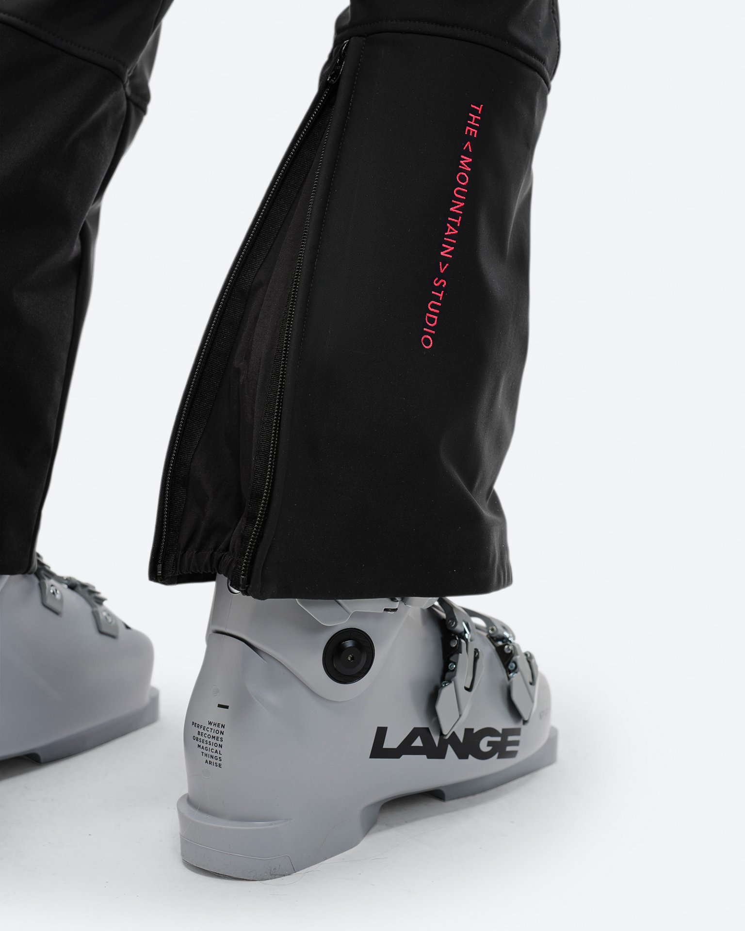 Black stretch ski pants Close-up of black stretch ski pants over a grey ski boot with zipper and brand logo.