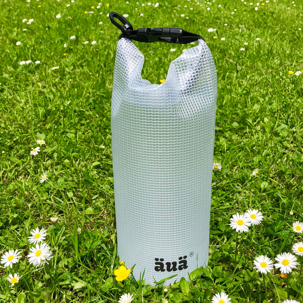 Dry bag transparent sur herbe verte avec des marguerites, avec fermeture noire et logo.