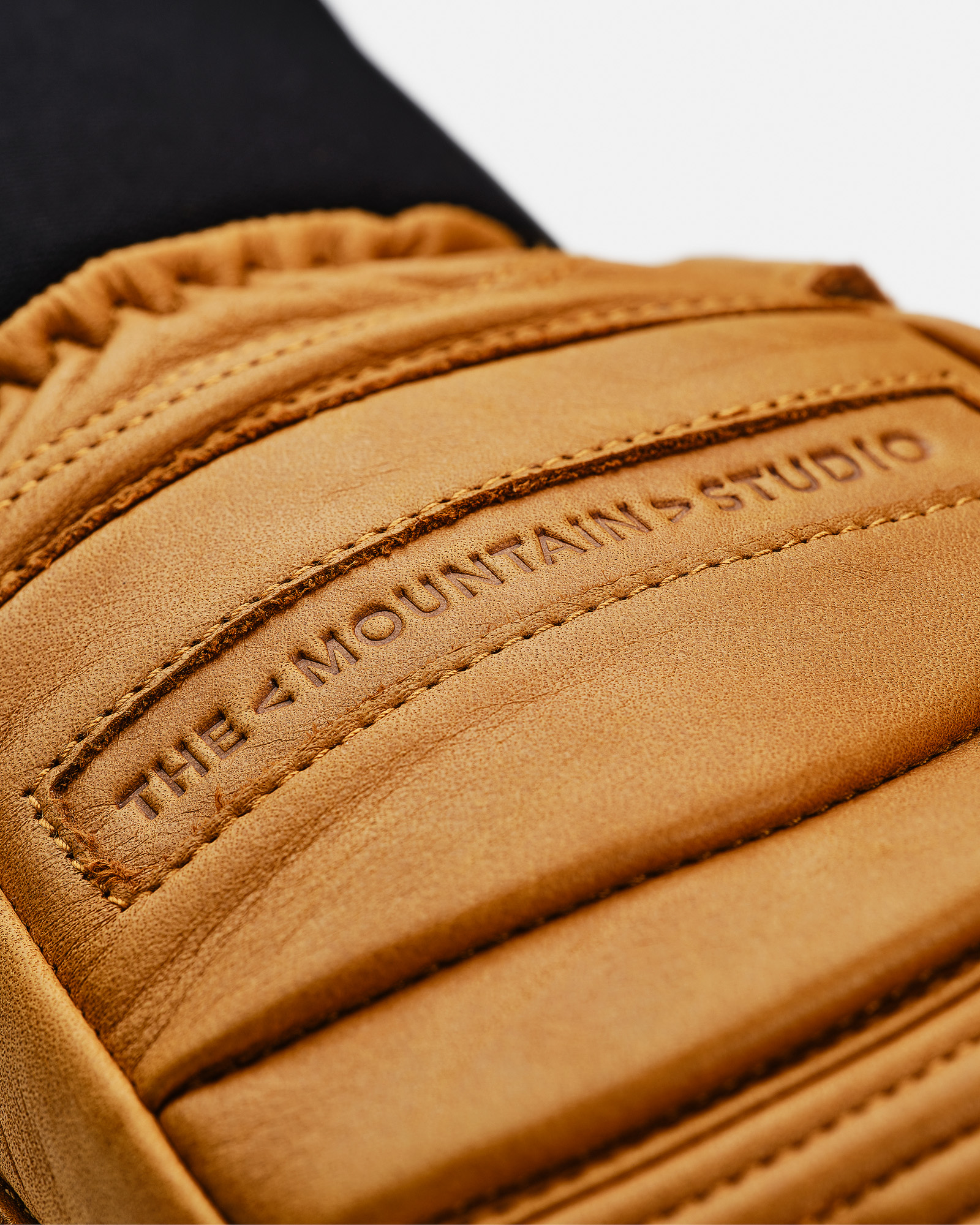 Leather glove sand color Close-up of a leather glove in sand color with "THE MOUNTAINS STUDIO" embossing and quilting details.