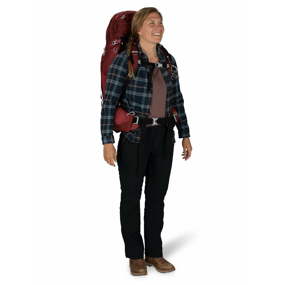 Lächelnde Frau mit blondem Zopf trägt einen roten Osprey Aura AG 65 Trekkingrucksack, speziell für weibliche Anatomie. Er sitzt optimal und zeigt das AntiGravity Rückensystem für maximalen Komfort auf langen Touren.