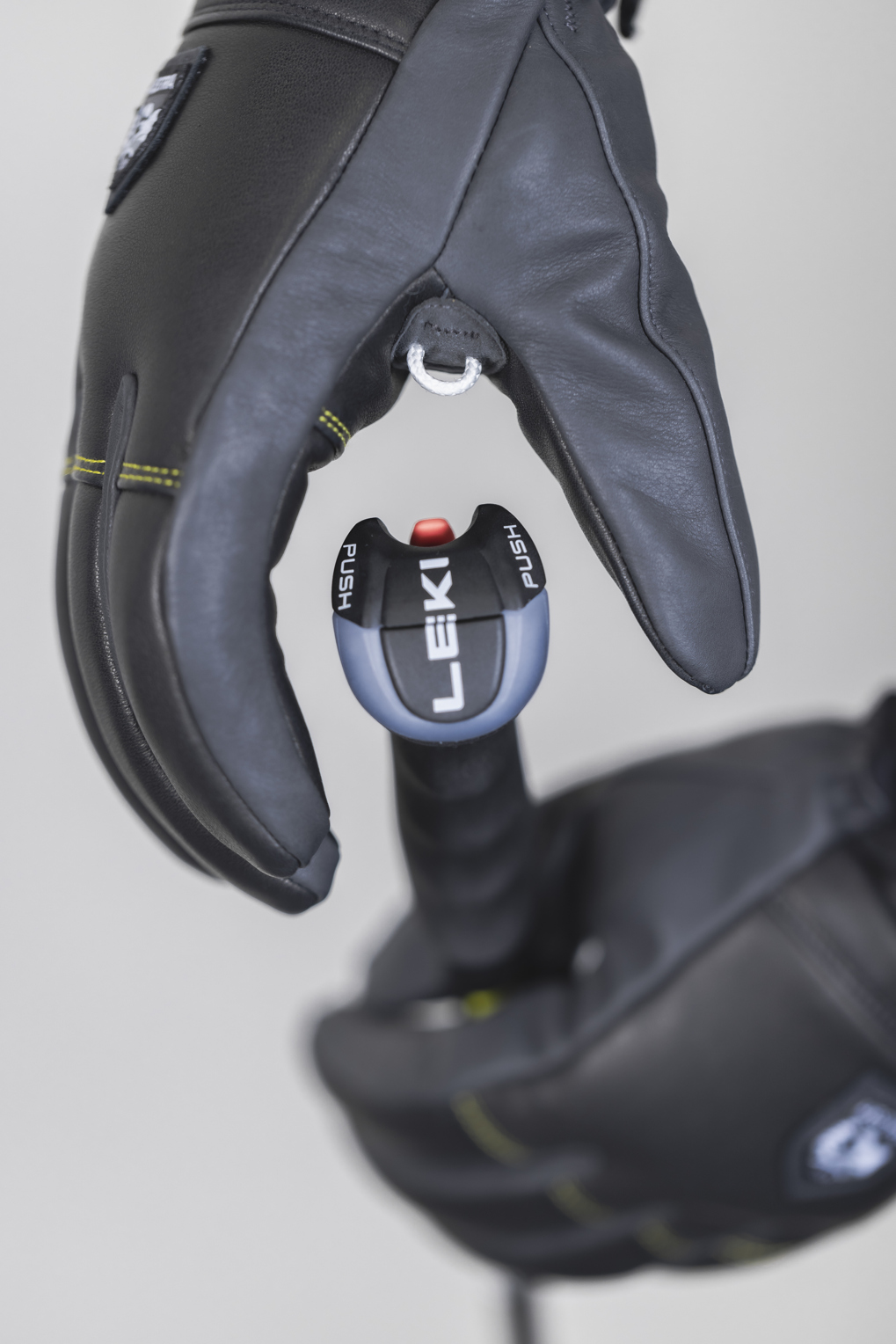Eine Hand in einem schwarzen Lederhandschuh hält einen Ski Stock mit dem Knopf "LEKI Push".