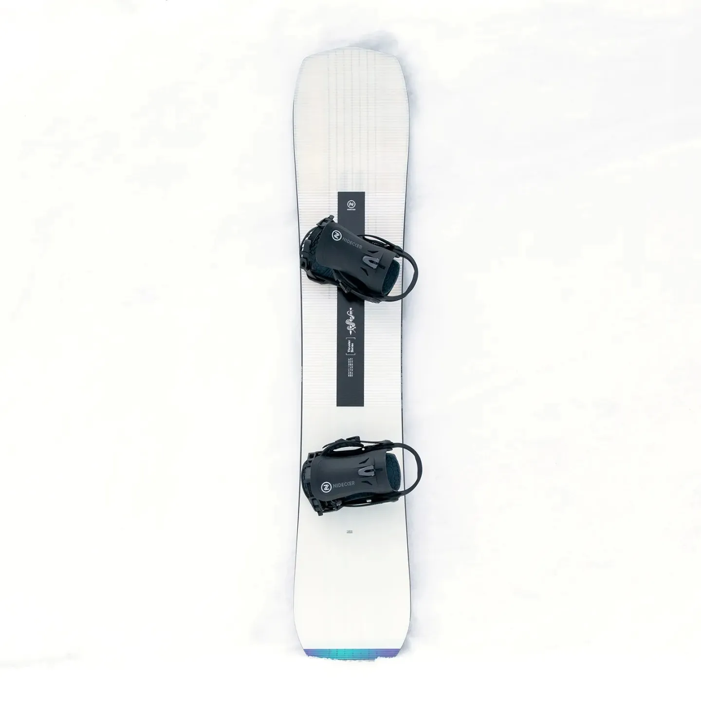 Vue de dessus du snowboard Nidecker Thruster dans la neige. La planche est blanche avec des fixations et des graphismes noirs.