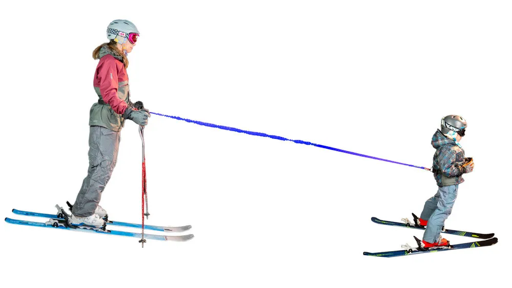 Skifahrende Frau und Kind durch blaues Seil verbunden. Frau trägt Tow-Whee Hüftgurt und zieht Kind auf Skiern.