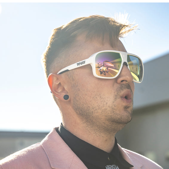Mann mit Sonnenbrille Mann mit weißer Sonnenbrille, Flugzeug spiegelt sich in den Gläsern. Er trägt einen hellrosa Blazer.