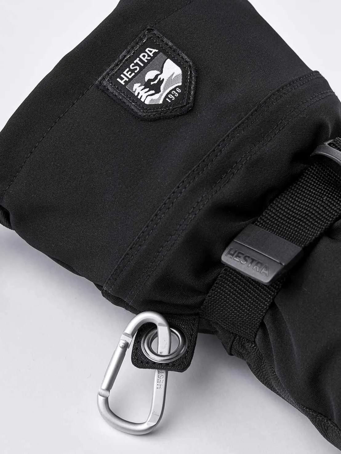 Primo piano di una muffola Hestra Army Leather Extreme nera con moschettone e logo.