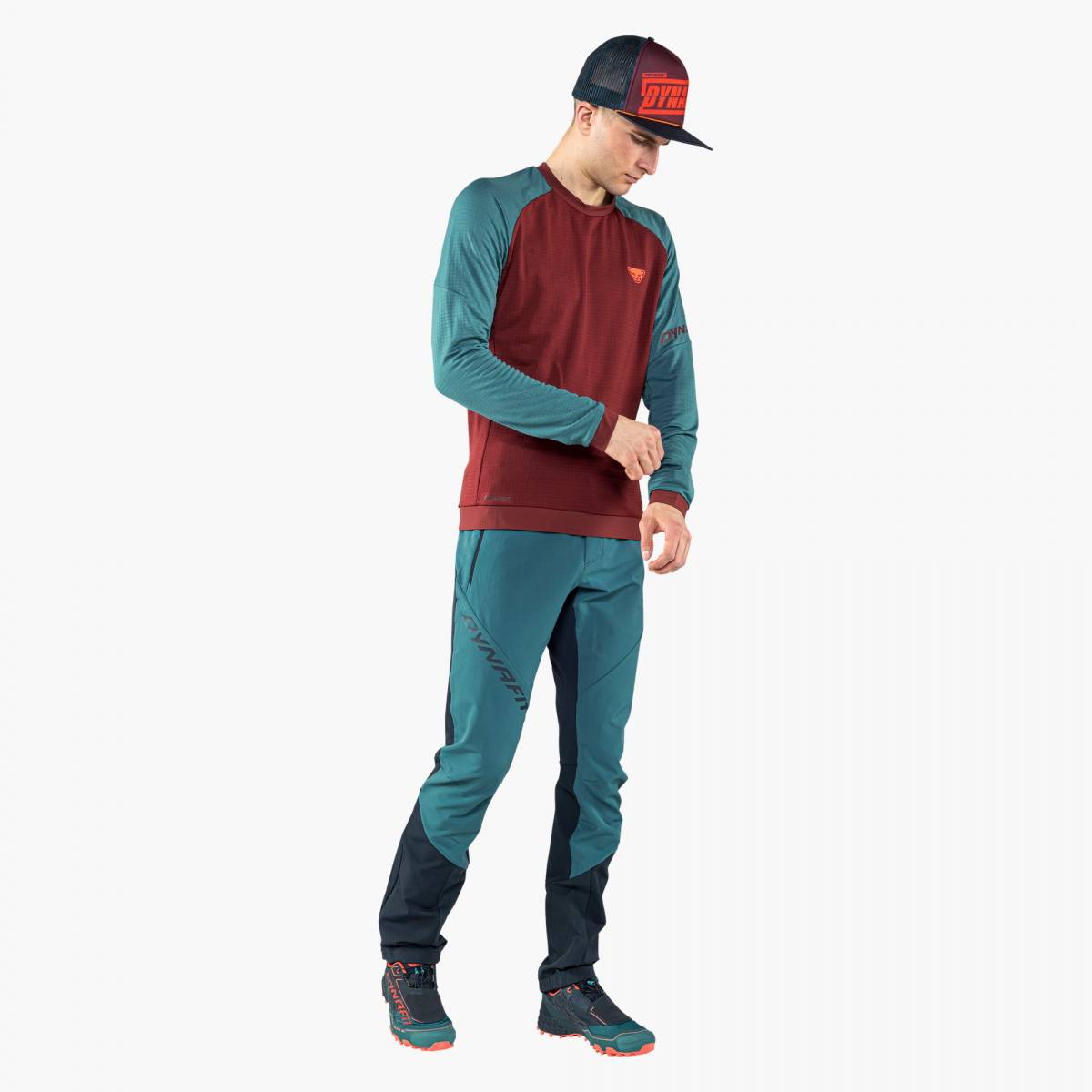 Man with Dynafit clothing, wearing graphic trucker cap in Syrah, looking down.