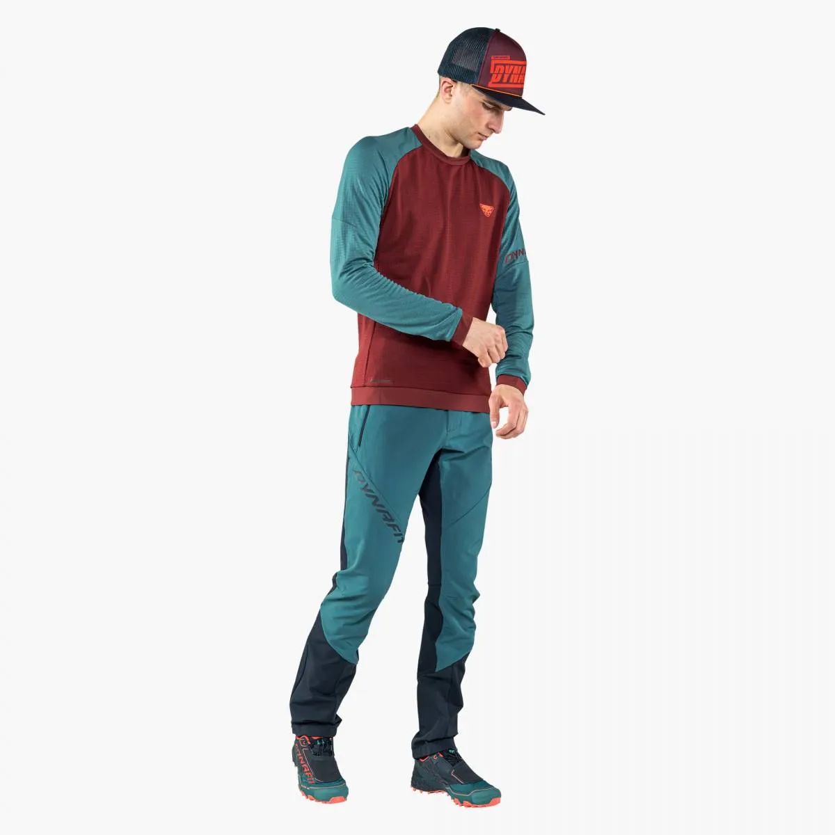 Man with Dynafit clothing, wearing graphic trucker cap in Syrah, looking down.