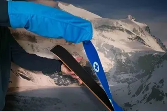 Hand pulls blue ski skin stocking over a ski skin in front of a mountain backdrop.