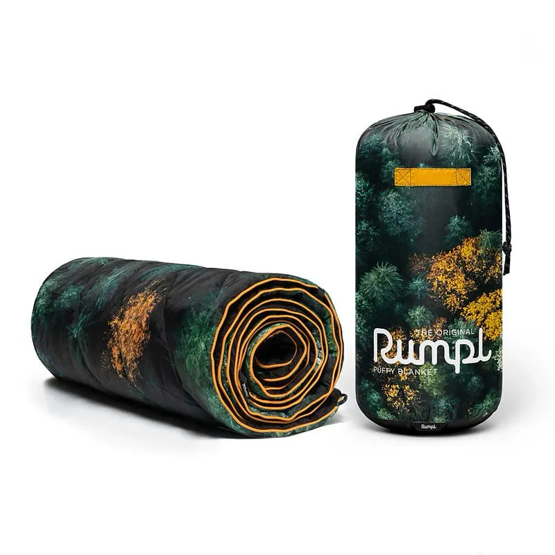 Gerollte Rumpl Puffy Blanket mit Waldmuster neben passendem Packsack.