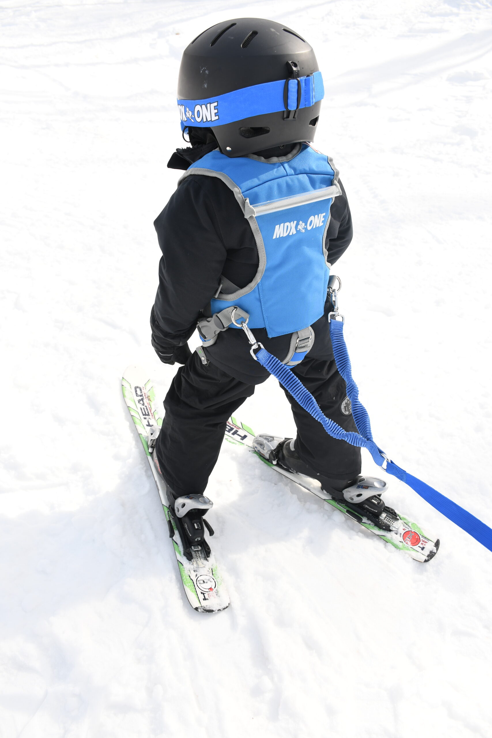 Boy skiing with helmet and blue harness on snow. Blue ropes are attached to the harness.