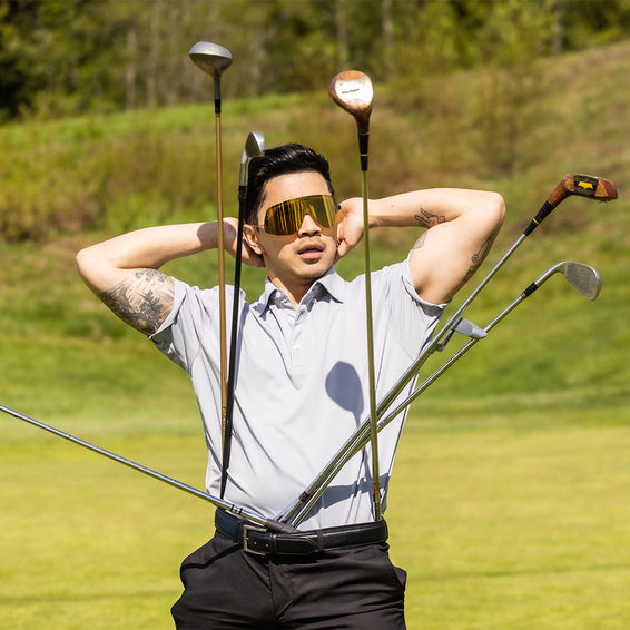 Mann mit Gold-Sonnenbrille, Golfschläger im Gürtel, Hände hinter dem Kopf.