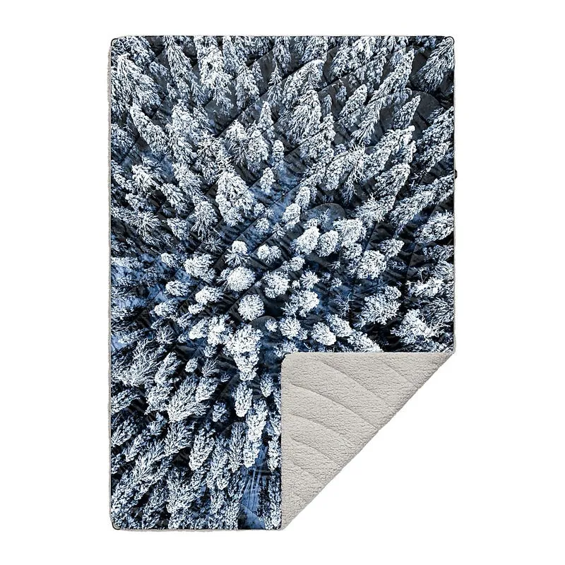 Rumpl Sherpa Decke mit Muster einer verschneiten Baumwipfel-Landschaft und beigem Sherpa-Fleece.