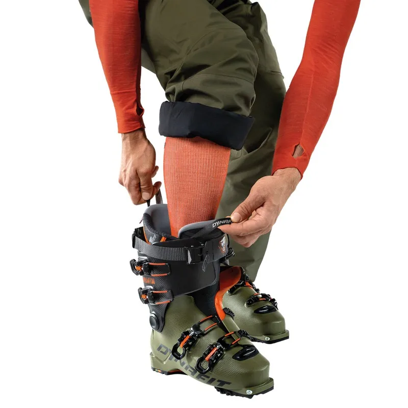 Personne met Dynafit Tigard Alpine Tech Chaussure de ski de randonnée. La chaussure de ski est verte et noire avec des accents orange.