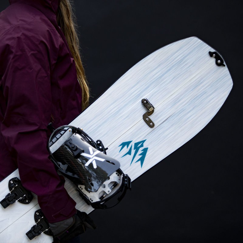 Jones Frauen Splitboard Person hält Jones Womens Solution Splitboard mit montierter Bindung vor schwarzem Hintergrund.