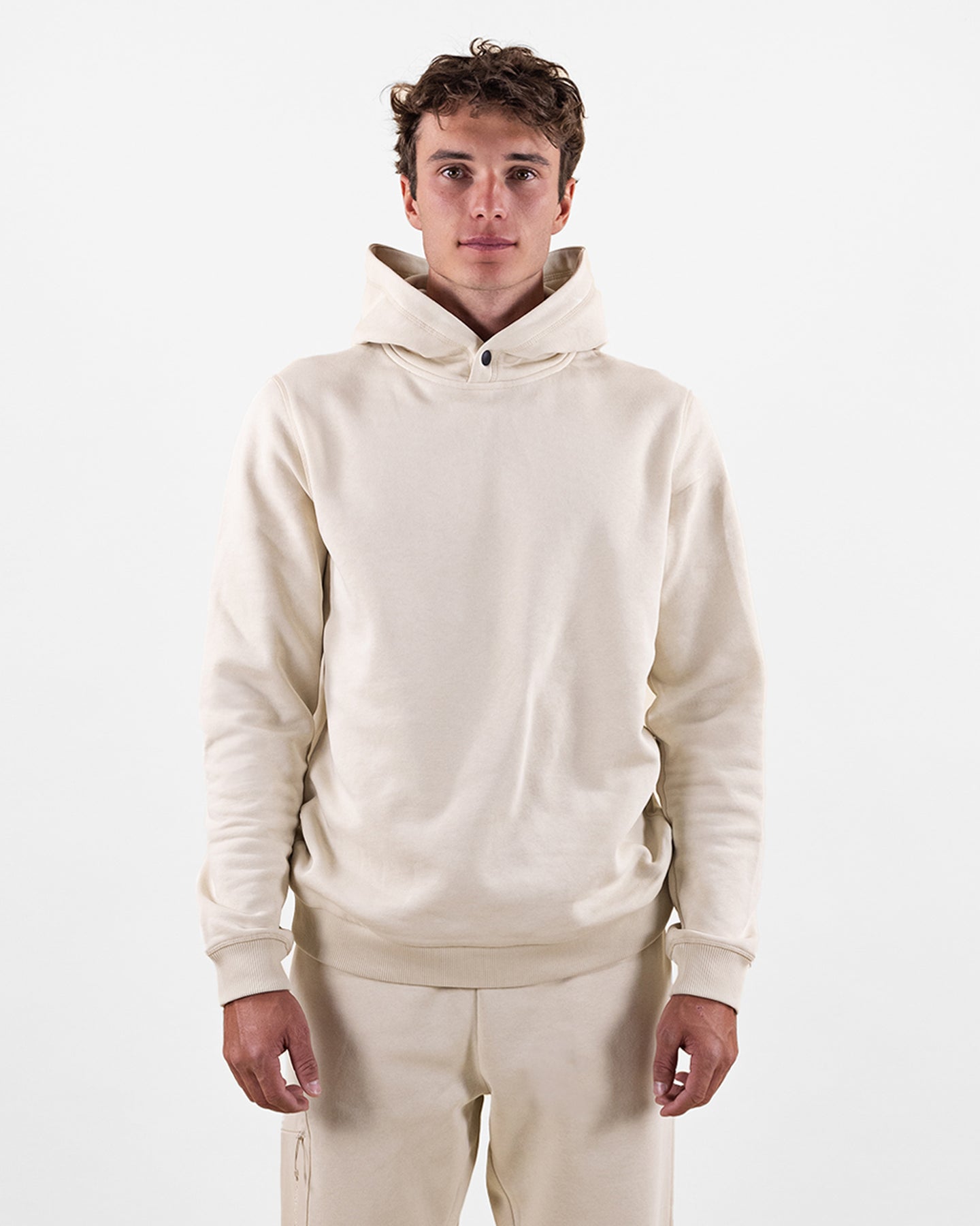 Uomo con felpa con cappuccio beige e pantaloni coordinati su sfondo bianco.