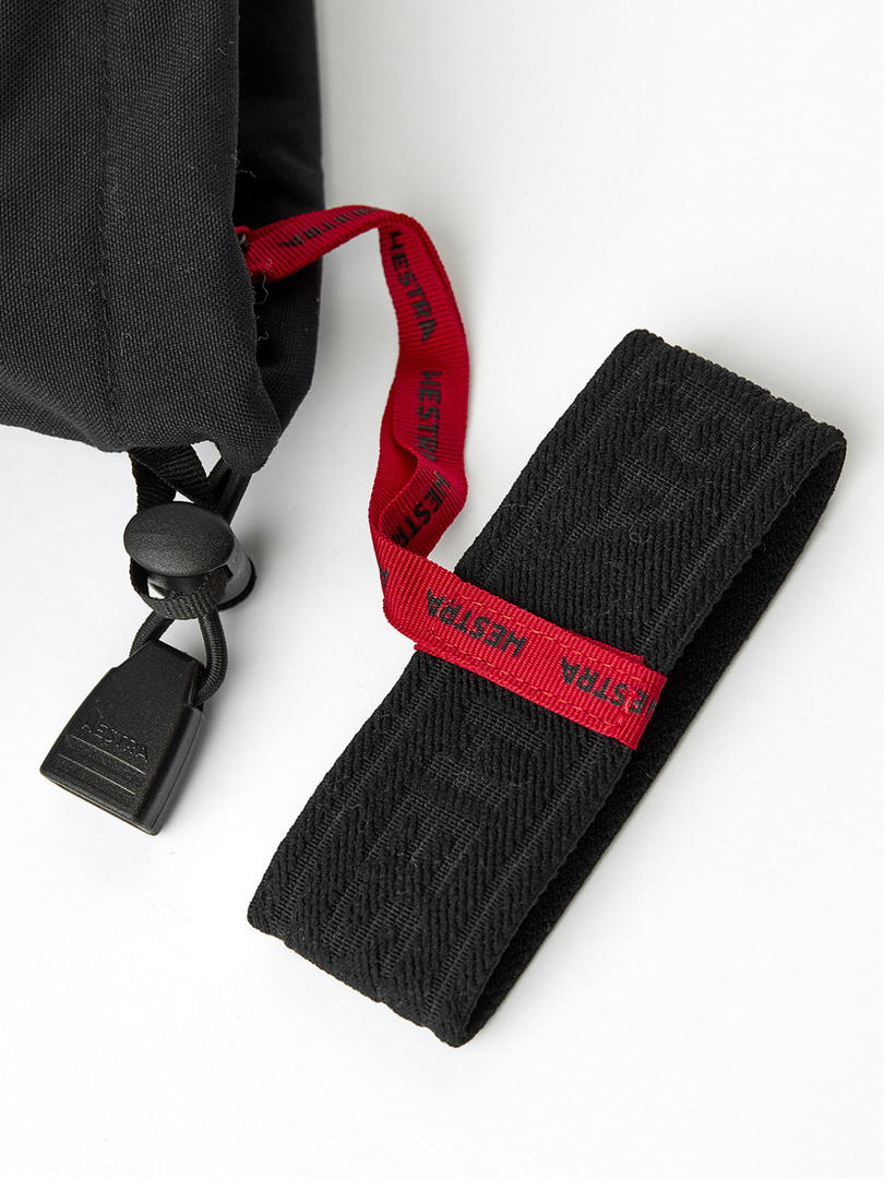 Detailaufnahme eines schwarzen Handschuhs mit Zugband und Band, jeweils mit rotem Band mit dem Aufdruck "HESTRA".