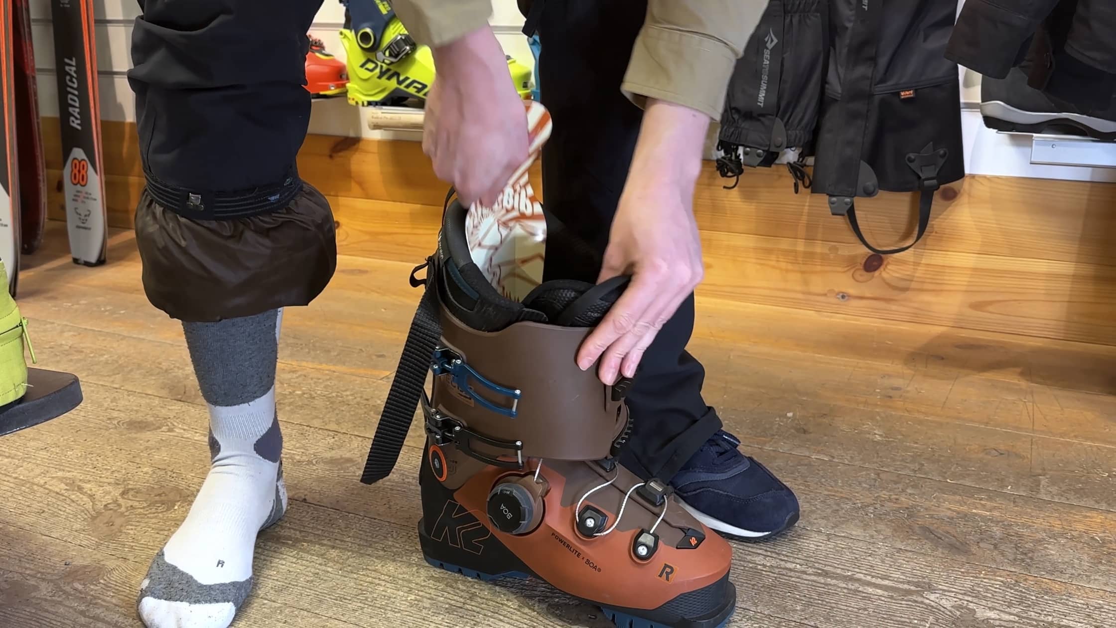 Person setzt einen Skischuh an. Brauner K2 Powerlite Skischuh mit Boa System wird angezogen. Socken und Gamaschen sind sichtbar.