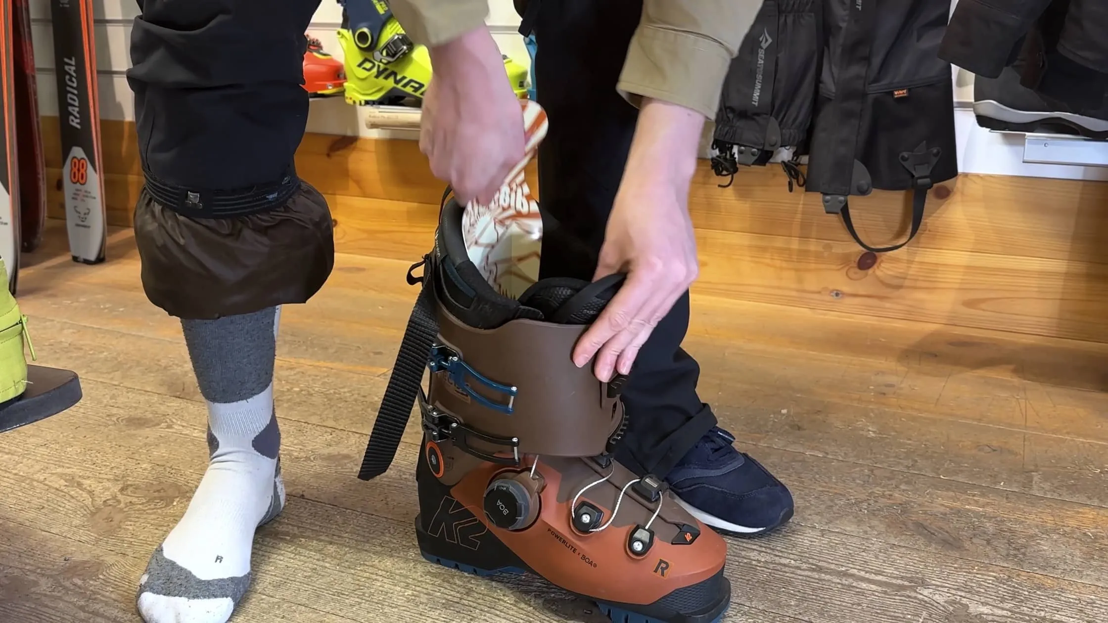 Person setzt einen Skischuh an. Brauner K2 Powerlite Skischuh mit Boa System wird angezogen. Socken und Gamaschen sind sichtbar.