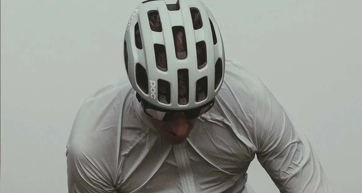 Ein Mann mit Sonnenbrille und weißem Velohelm der Marke POC schaut nach unten. Er trägt eine helle Jacke.