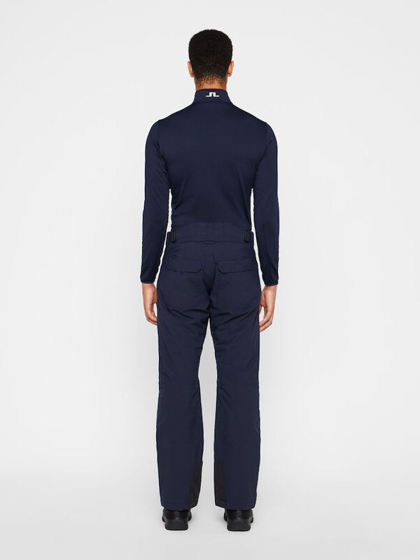 Rückansicht einer Person in marineblauen Truulli Skihose und Oberteil von J.Lindeberg vor einem weißen Hintergrund.