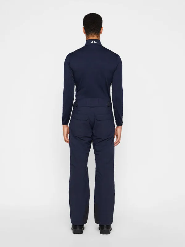 Vista posteriore di una persona con pantaloni da sci Truulli blu navy e top di J.Lindeberg su sfondo bianco.