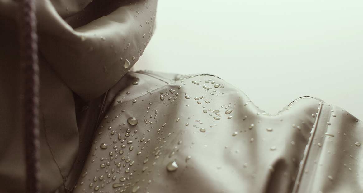 Wasserabweisende Kapuzenjacke Nahaufnahme einer wasserabweisenden Jacke mit Kapuze, auf der Wassertropfen liegen.