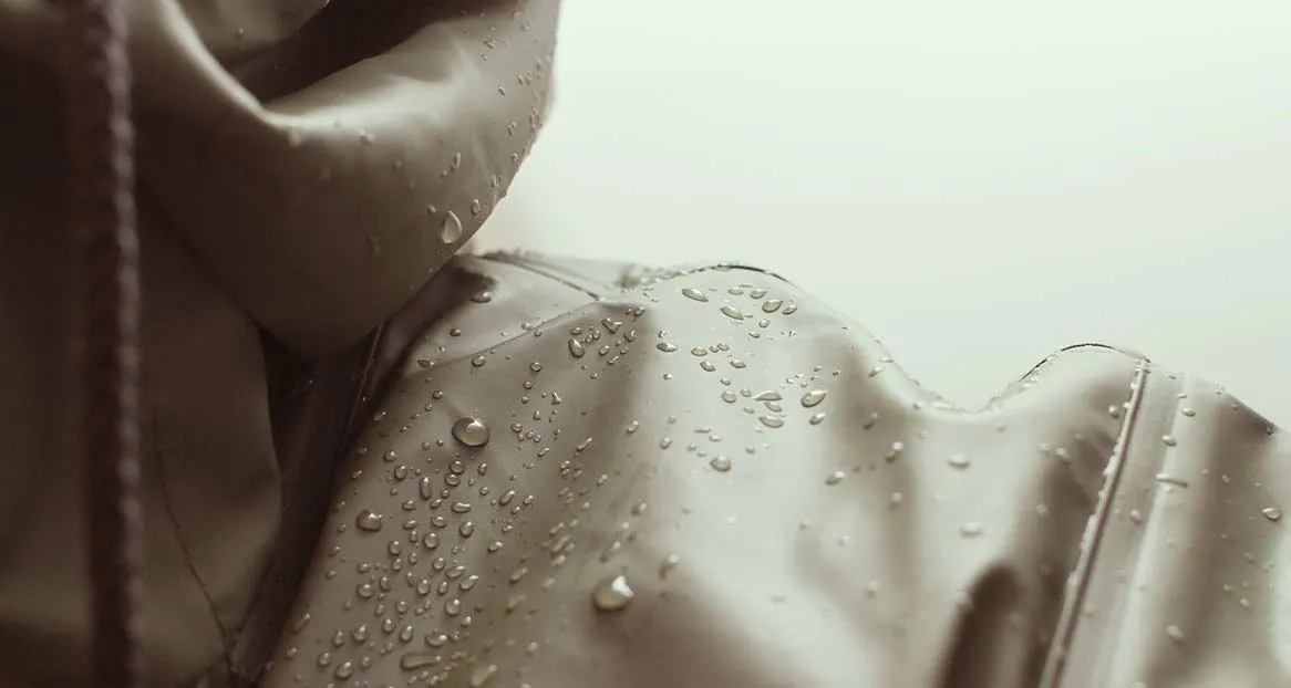 Nahaufnahme einer wasserabweisenden Jacke mit Kapuze, auf der Wassertropfen liegen.